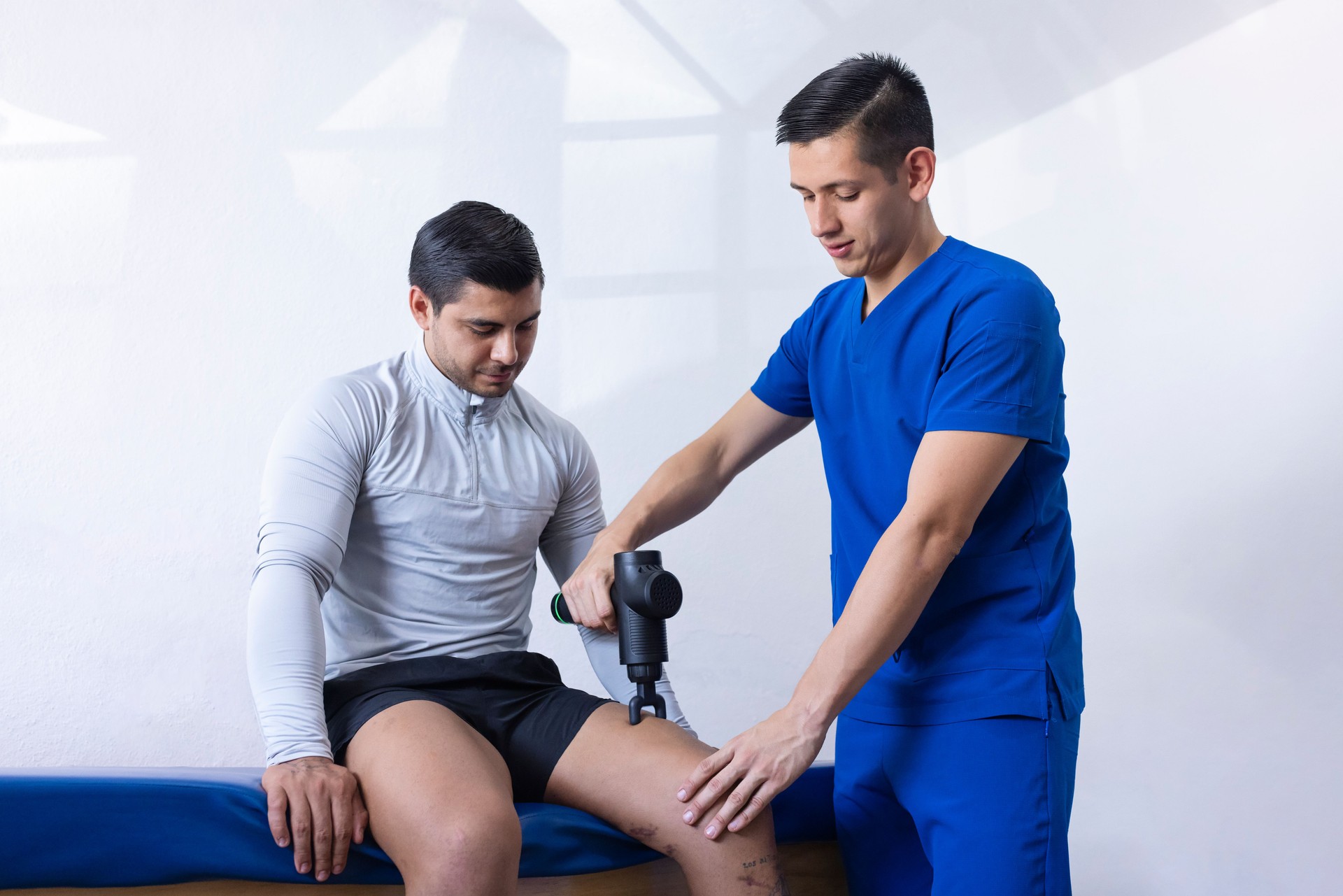 Physiotherapist using a leg massage gun on an athlete's leg